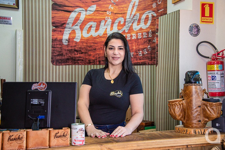 Mulher branca de cabelos pretos em pé e sorrindo em sua loja especializada em erva-mate em Umuarama