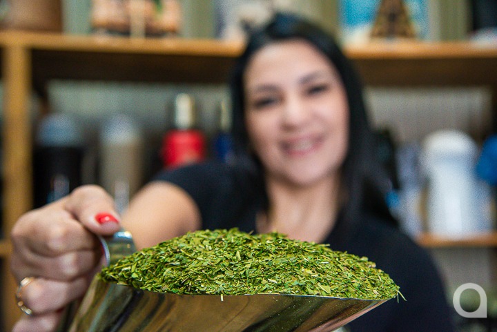 Mulher branca de cabelos pretos sorrindo e segurando uma medida do produto em sua loja especializada em erva-mate em Umuarama