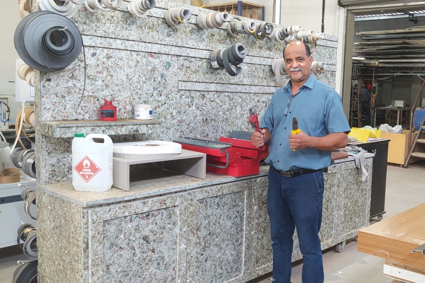 Homem branco em pé ao lado de um móvel construído com as caixinhas de leite.